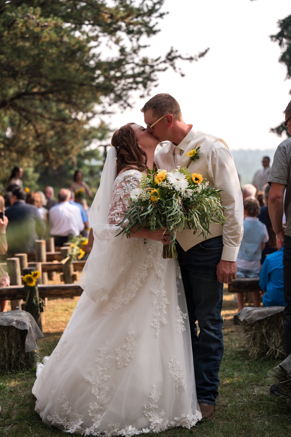 wedding couple kissing in the middle of all of their guests, bride is holding a boquet of sunflowers