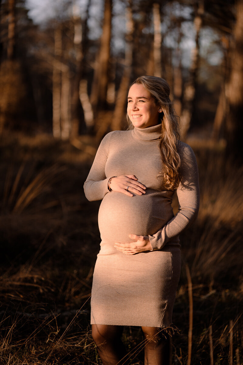 zwangere vrouw staat in de zon te genieten van de zon en heeft haar handen rondom haar buik