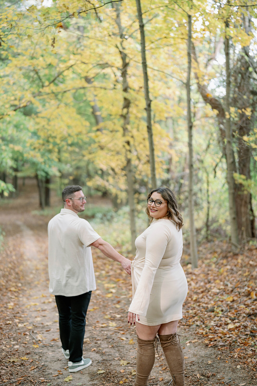 Couple walking hand in hand through the trees at Al Sabo Preserve with golden fall leaves surrounding them.