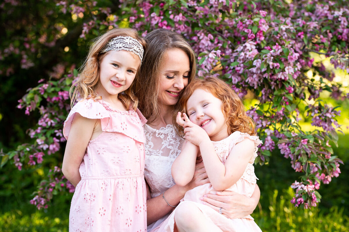 Ottawa family photography of a mom hugging her daughters in the blossoms at the Arboretum