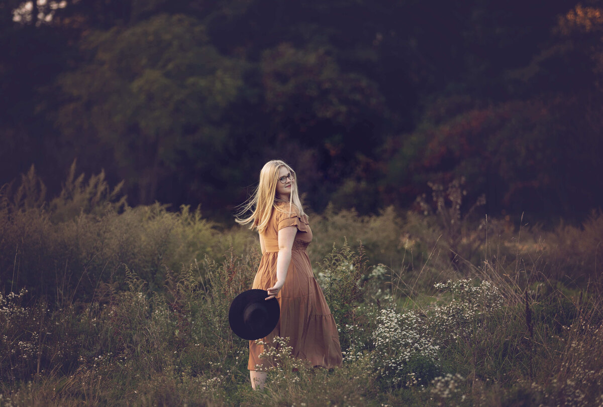 Senior portrait of a girl walking through wildflowers looking back at photographer in Erie Pa field
