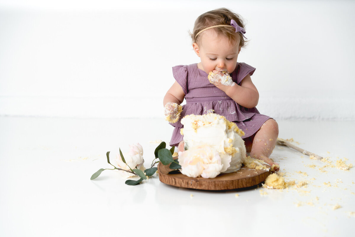 A baby girl is eating cake in a photography studio.