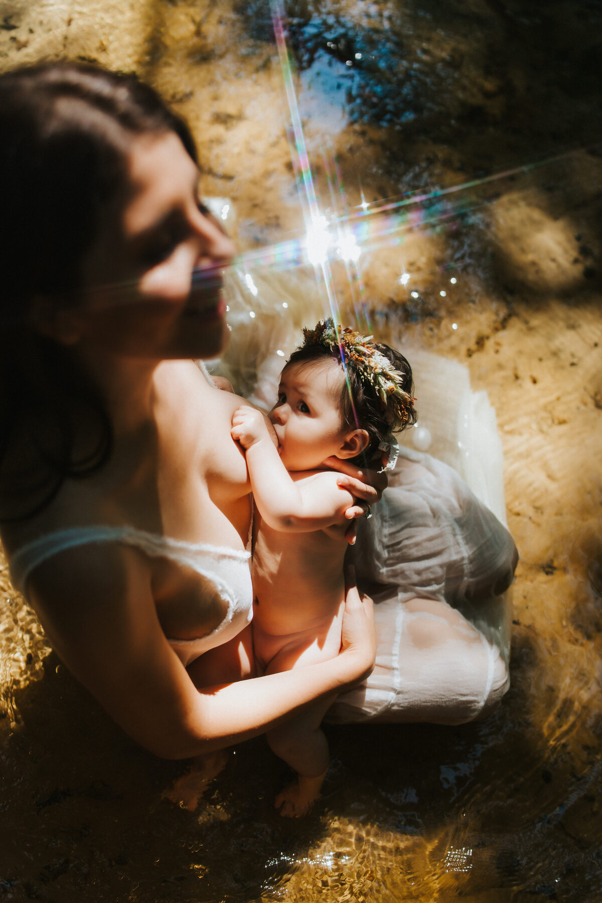 stunning artistic creek portraits of a women sitting in a creek breastfeeding her baby