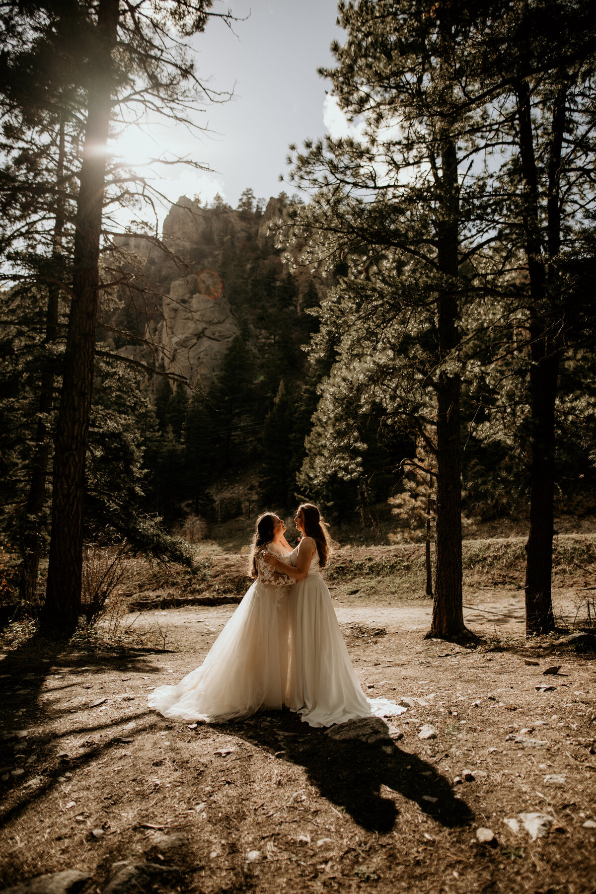 same sex female couple holding each other in bridal gowns with sun behind them