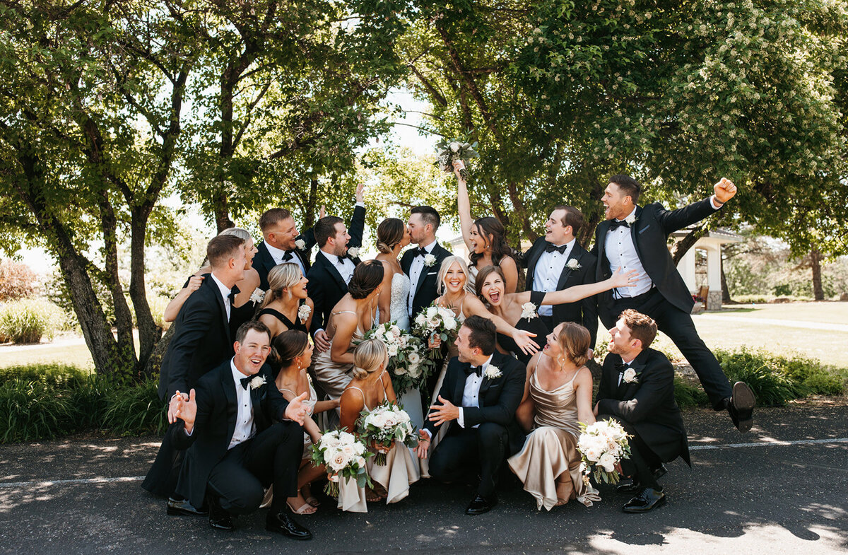 Group photo of bride and groom kissing while their wedding party celebrates around them