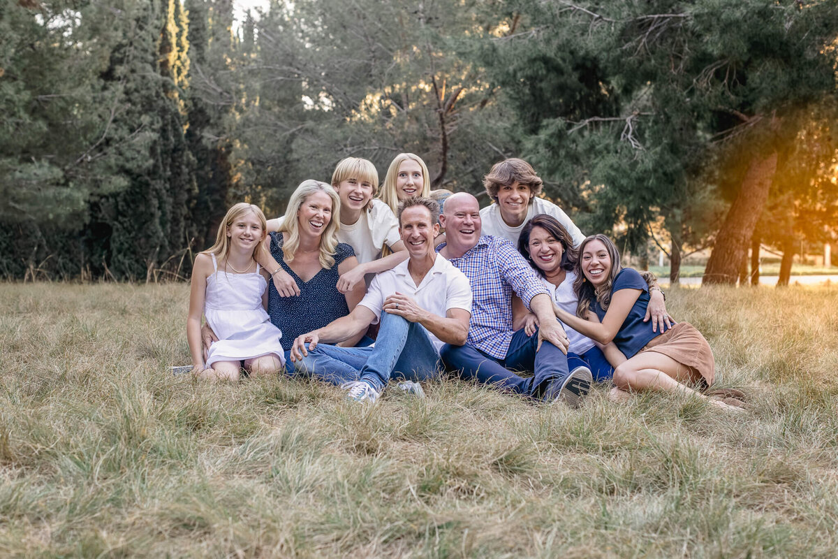 A large family with their arms around each other, smiling at the camera and sitting in the grass surrounded by trees at Jeffrey Open Space.