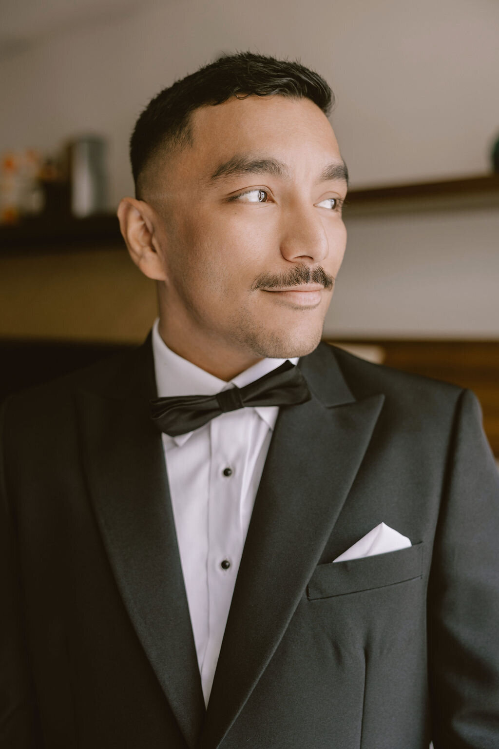 groom portrait looking out a window wearing a tuxedo in laylow waikiki hotel room