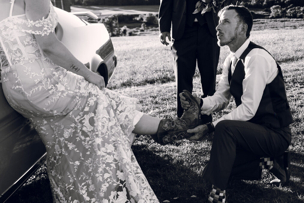 A bride is putting on her wedding shoes in front of a car.