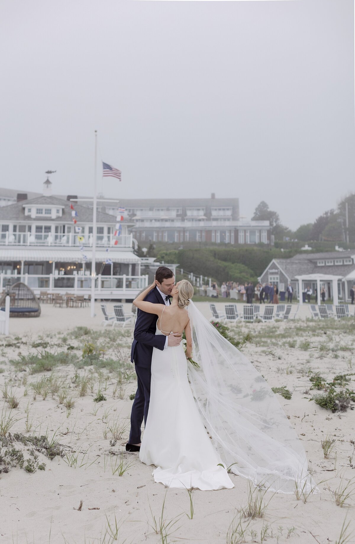 Bride and Groom kiss on beach in front of Chatham Bars Inn.
