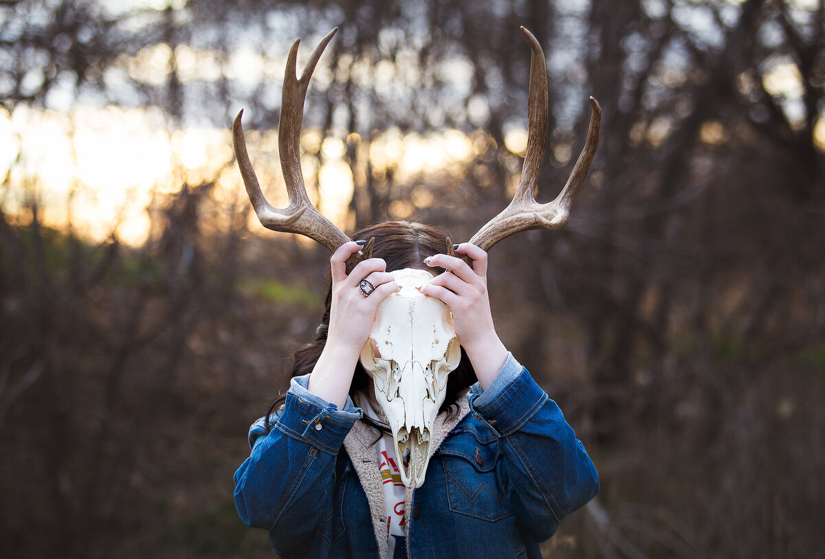 Western senior girl standing with deer skull in front of face