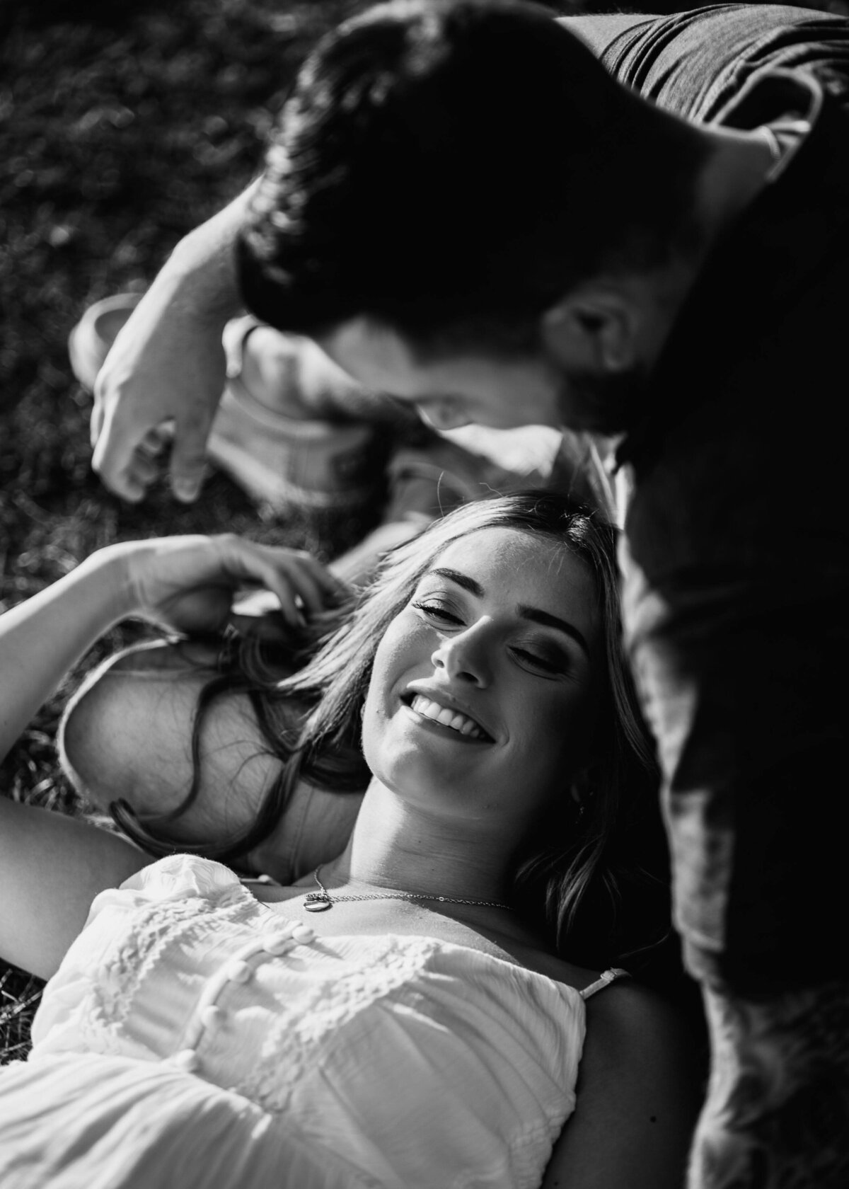 Black and white photo of a couple laying in the grass, captured by a Pittsburgh maternity photographer.