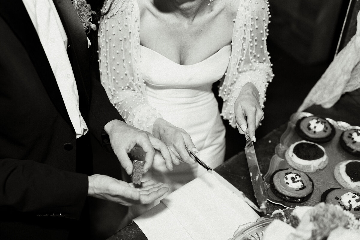 Destination wedding bride cutting cake in white beaded sleeve dress