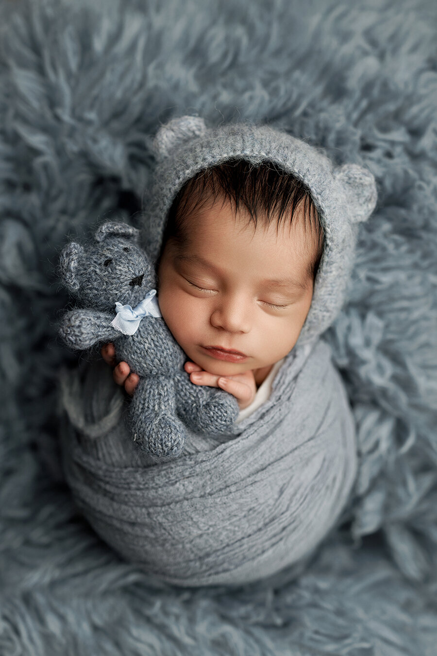 Denver newborn baby boy wrapped in blue laying on a rug holding a teddy bear.