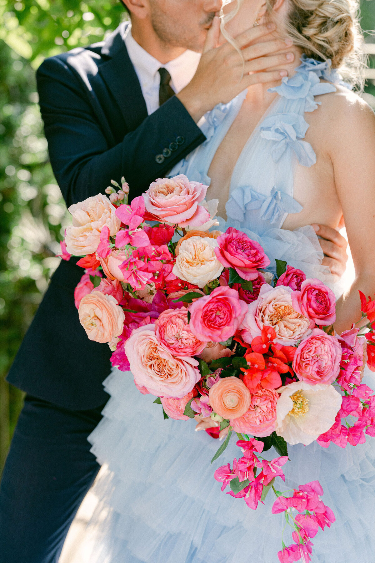 Couple kissing each other while girl holds a pink floral bouquets