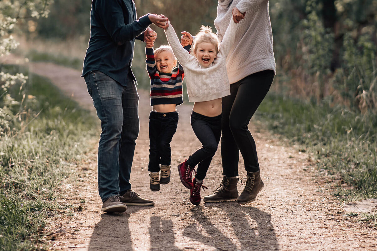 A cropped in photograph of two preschool aged siblings laughing while being lifted in the air by their parents.