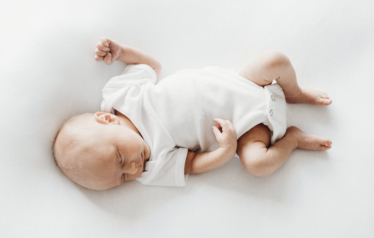 Newborn baby sleeping peacefully on a white sheet during a natural light Kansas City newborn photography session.