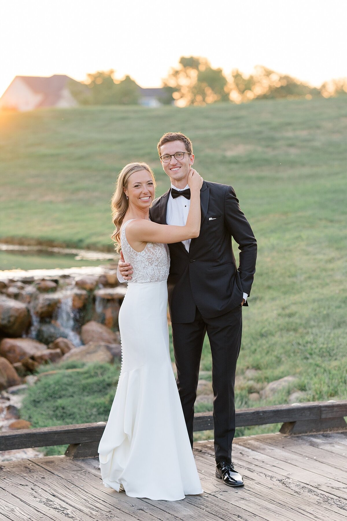 Pinnacle wedding photos with bride and groom standing on a bridge on the golf course and posing as the sun sets over the small waterfall behind them
