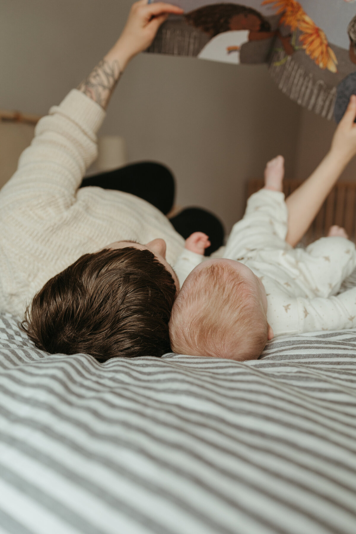 mom and baby girl holding book up in the air and reading book-camera is looking at the top of their heads during in home family session in longmont colorado