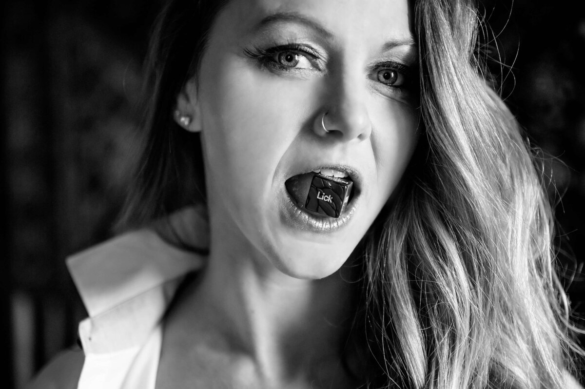 black and white photo of a woman with a dice in her mouth that says lick
