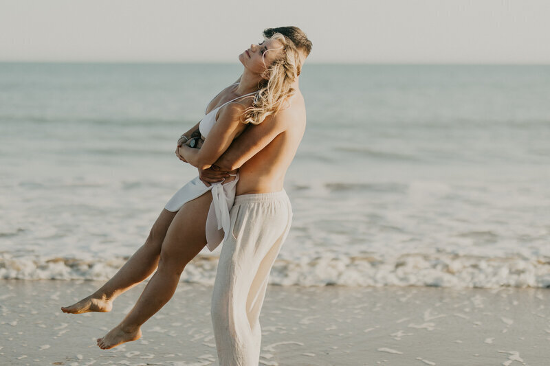 Homme réalisant un porté avec sa chéri à la plage lors d'une séance photo couple en Vendée.