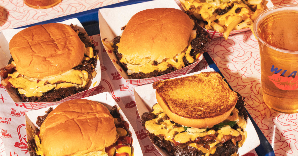 Smashburgers topped with cheese and sauce, fries with grilled onions, and a drink served on a branded tray at With Love, Always in Las Vegas