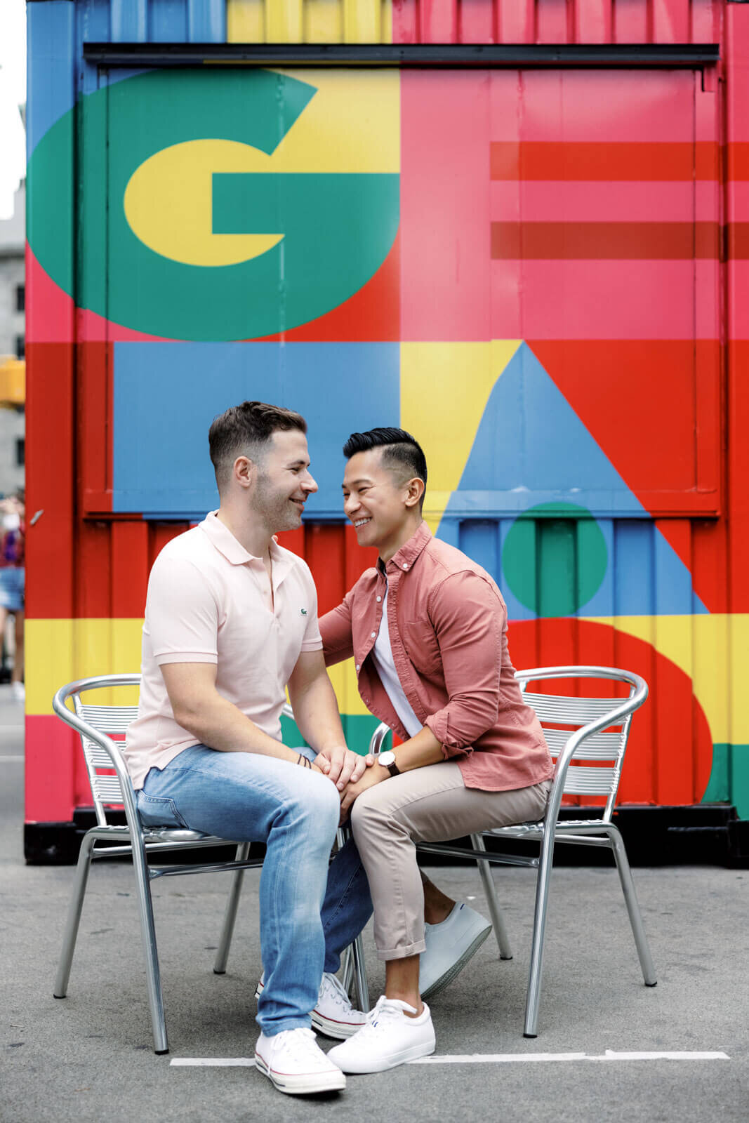 The engaged couple is happily sitting with a colorful wall in the background in West Village, NYC. Image by Jenny Fu Studio.