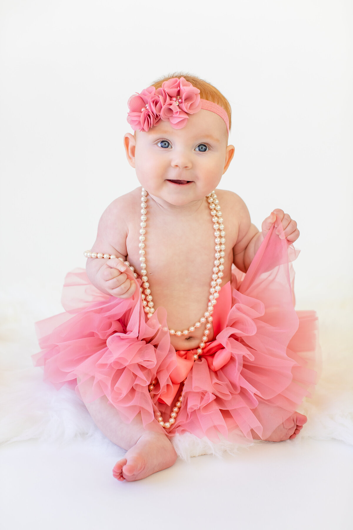 Baby girl in pink tutu and pearls smiling at camera