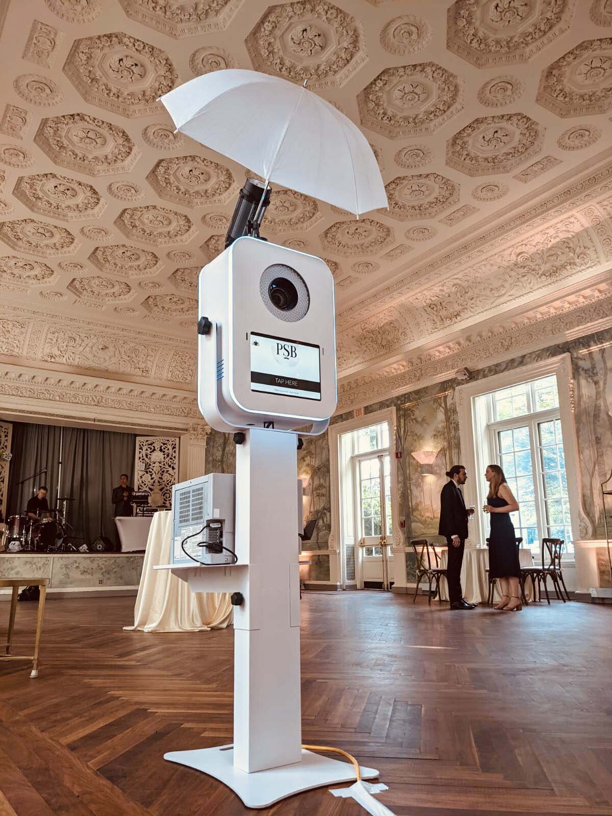 Sleek white photo booth placed in an ornate venue with tall windows and a decorative ceiling.