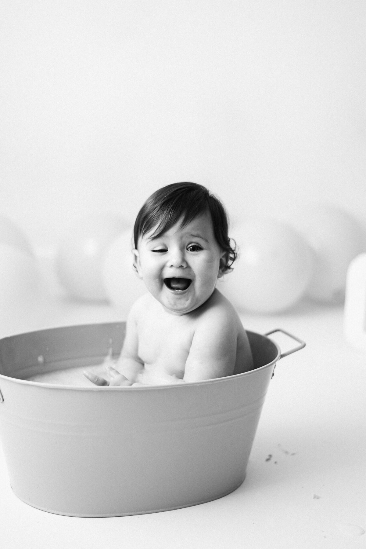 Baby girl sitting in a bath tub smiling at Billingshurst cake smash photoshoot