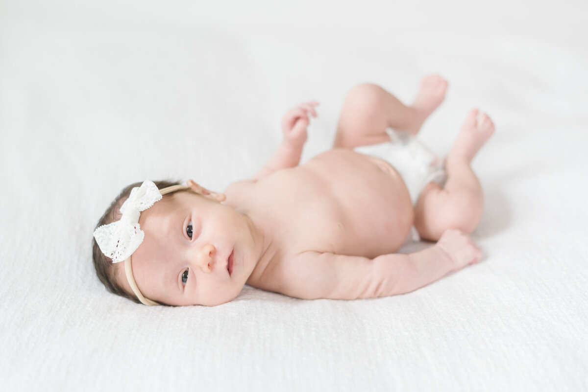 Baby laying on bed wearing diaper and headband - Washington DC Newborn Photographer