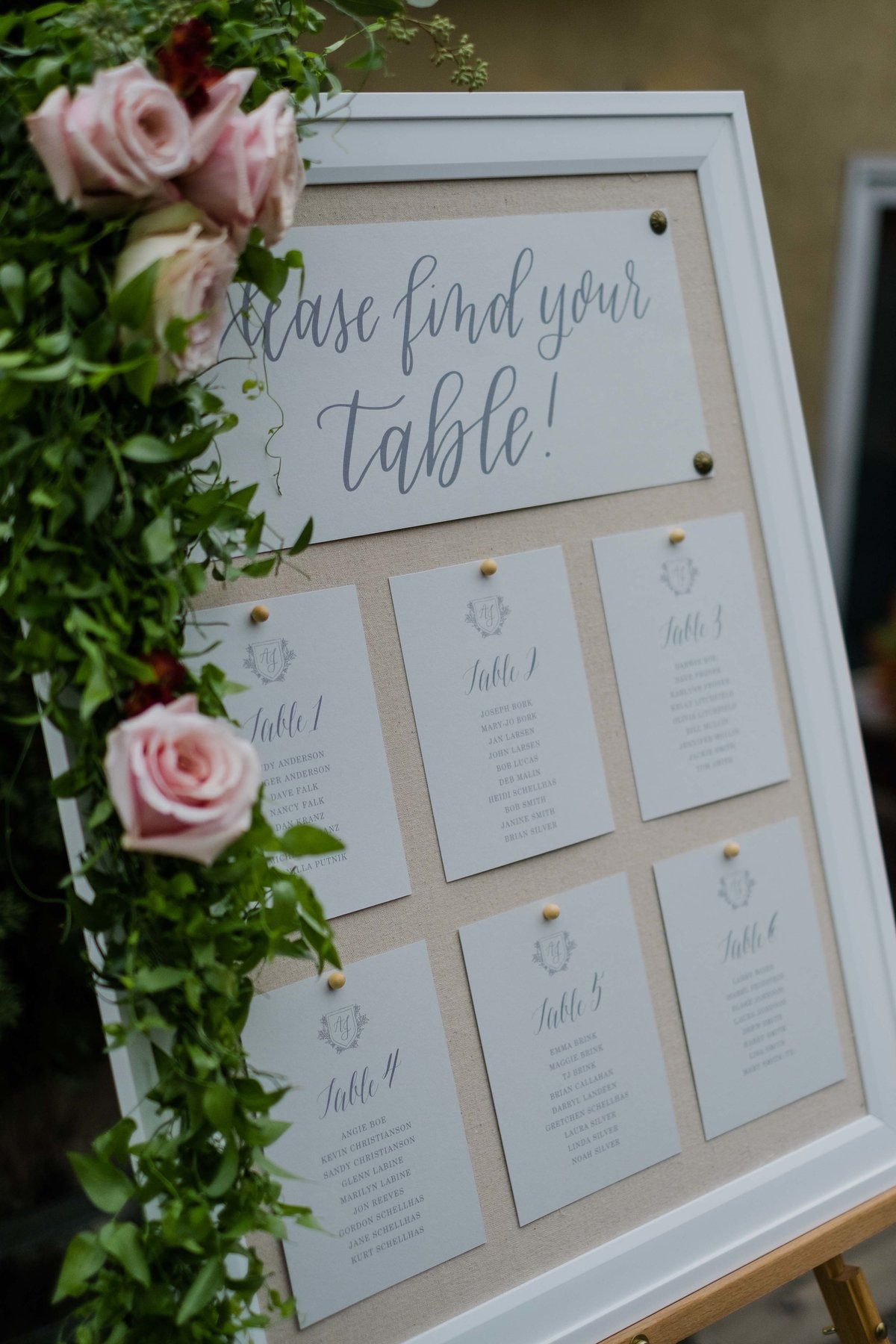 Calligraphy escort card board with smilax and roses decorating the frame.