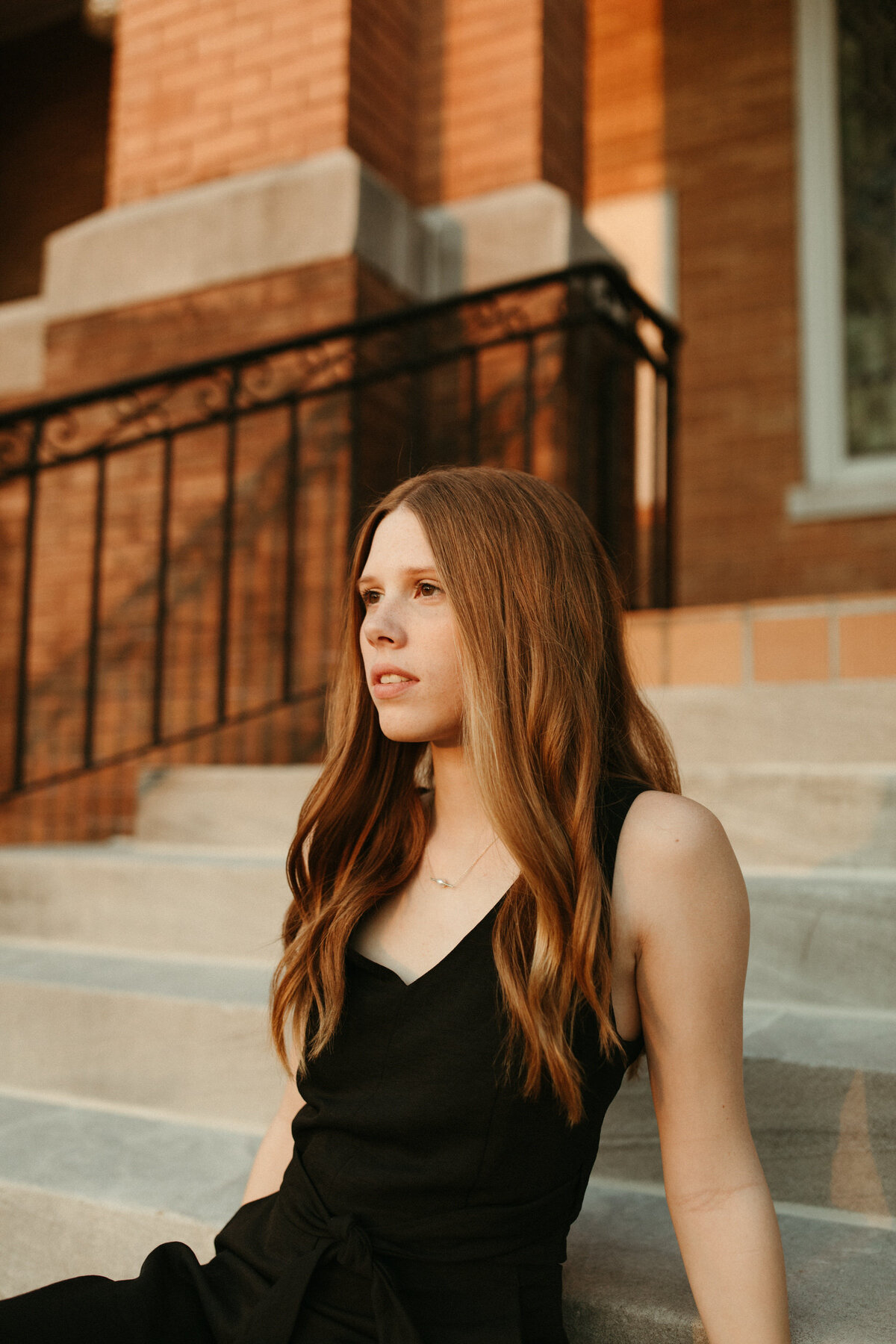 High school senior in a black jumpsuit sitting on the steps of a downtown church