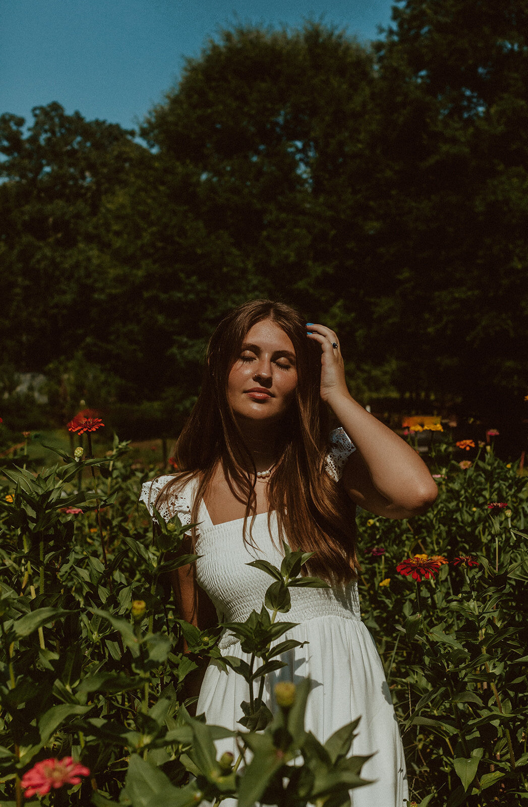 highschool senior stands in direct sun in field of flowers 