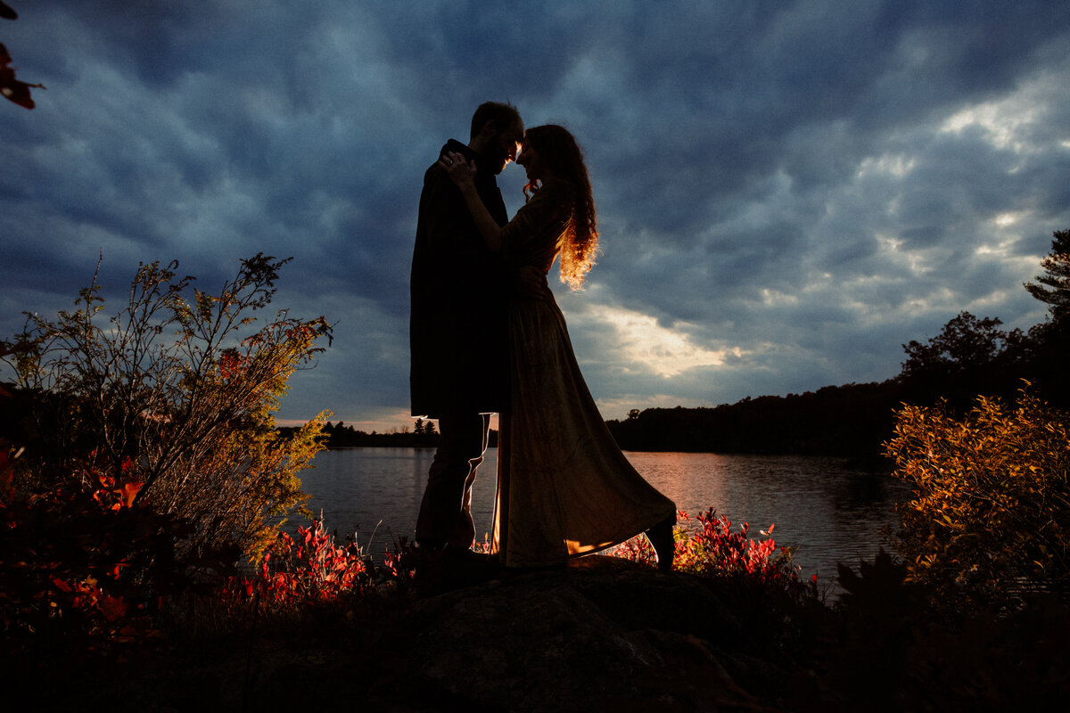 engaged-couple-backlit-by-a-dramatic-dark-sunset-sky-at-little-mellon-lake-ontario-1