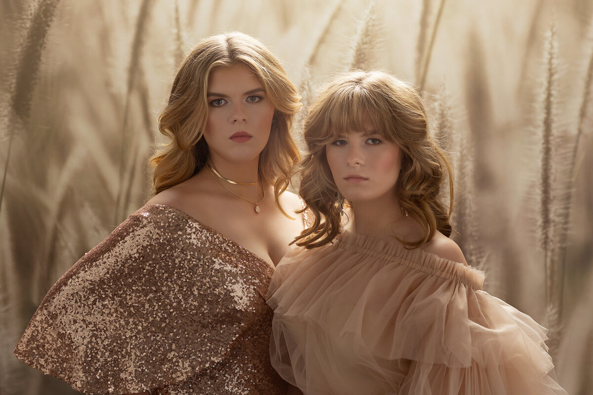 Two sisters pose against a soft, neutral background, exuding elegance in their stunning gowns. One wears a rose gold sequin dress, while the other is in a delicate blush tulle gown. Their sophisticated styling complements the dreamy atmosphere in this Dallas senior portrait session.