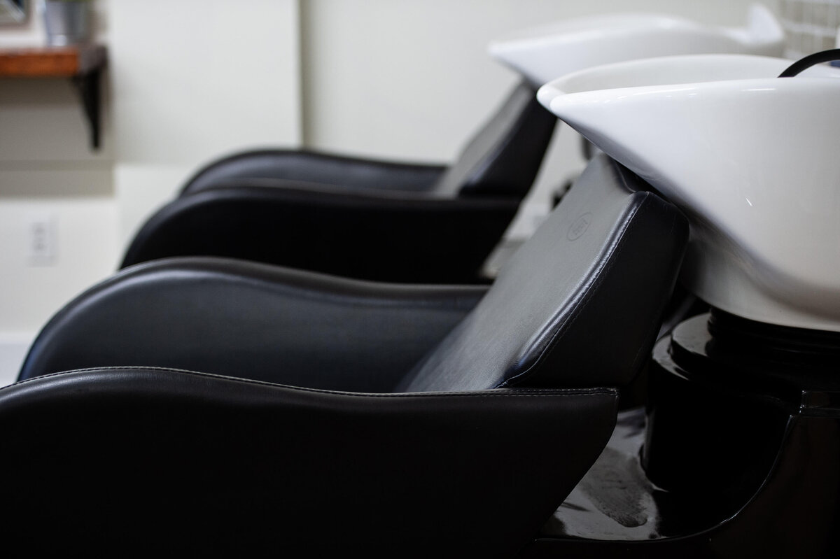 a photo of a hair wash station at a hair salon showing two black chairs and white sinks.  Captured on-location at Richardson Hair Design by Ottawa branding photographer JEMMAN Photography