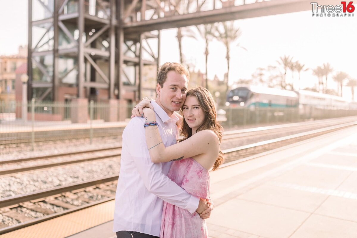 Engaged couple embrace one another next to the Fullerton Train Station tracks