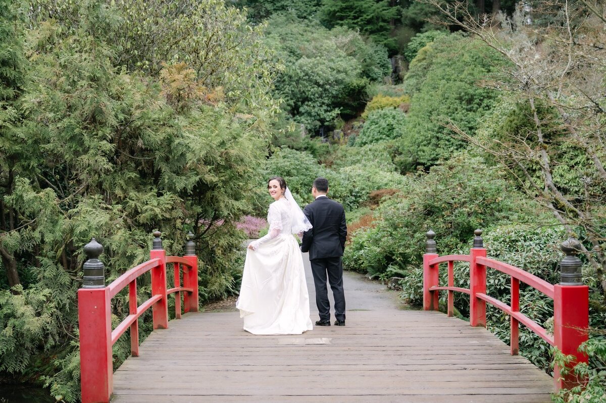 bride and groom walk across bridge at kubota garden away from camera