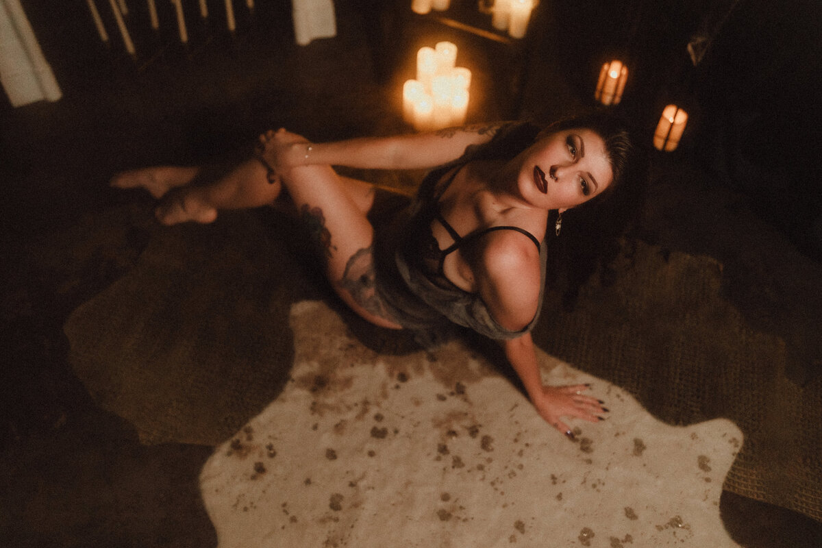 Woman sits confidently on floor with candles surrounding her, captured from above in dark, styled Florida studio boudoir shoot.