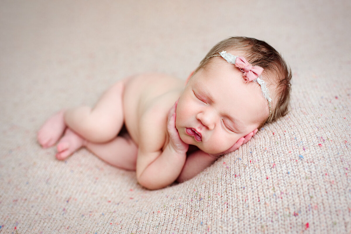 Newborn photography portrait of baby girl side lying with pink bow in Neptune Beach, FL.