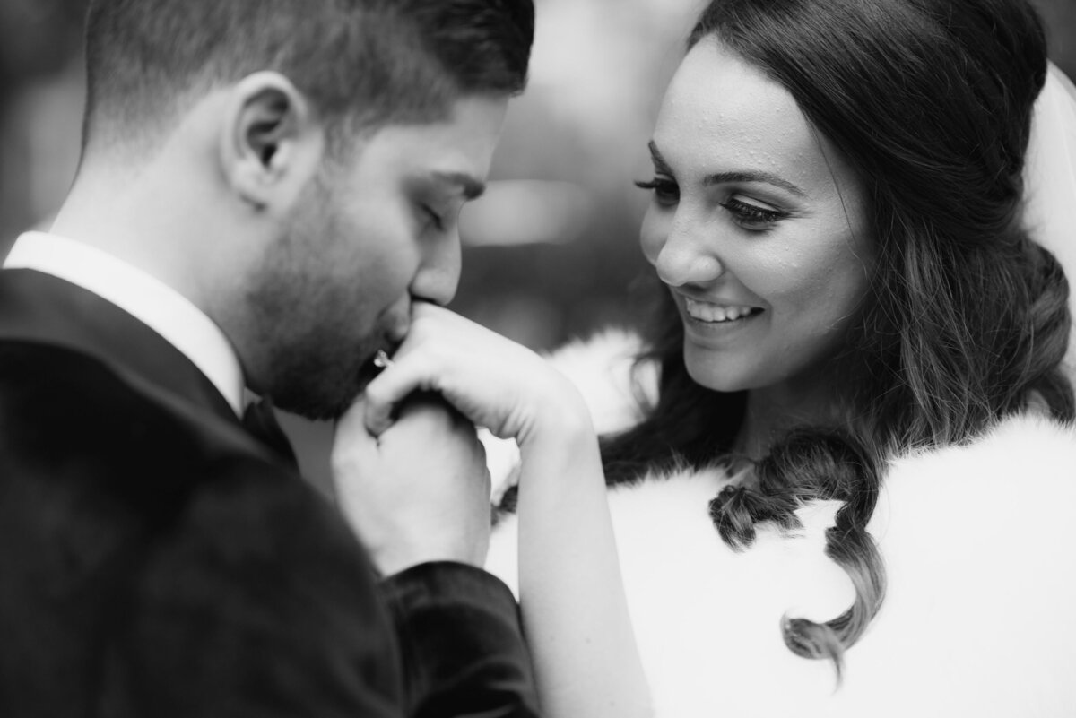 A timeless black-and-white photograph of a groom gently kissing his bride's hand, capturing a moment of pure affection and romance as they share a tender connection on their special day.