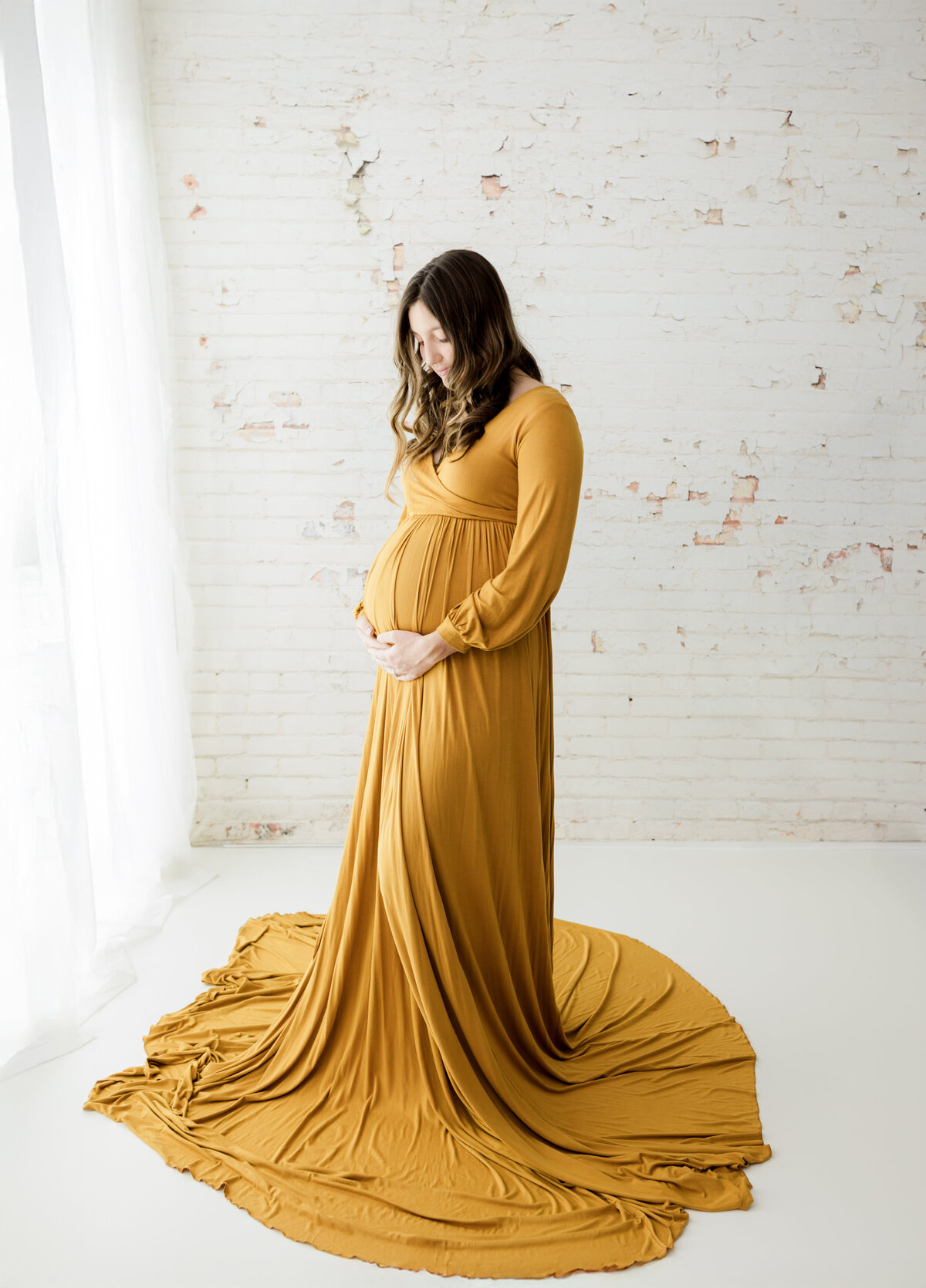 pregnant mother in gold maternity gown holding baby bump for studio maternity photoshoot