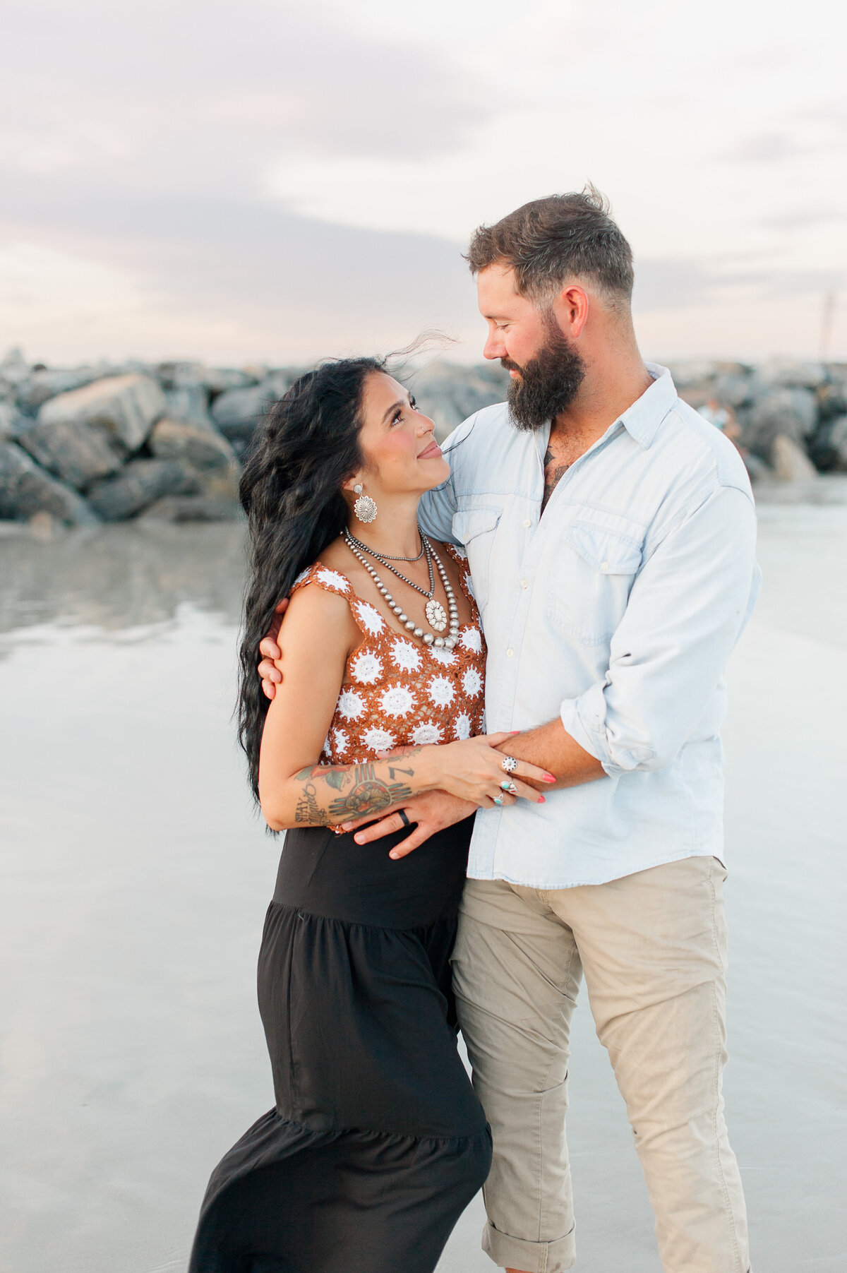 Parents standing in front of rocks on the beach smiling at each other