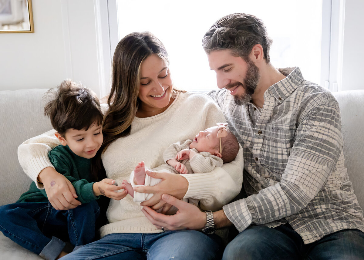 Lifestyle photo of parents and big brother posing with a newborn baby.
