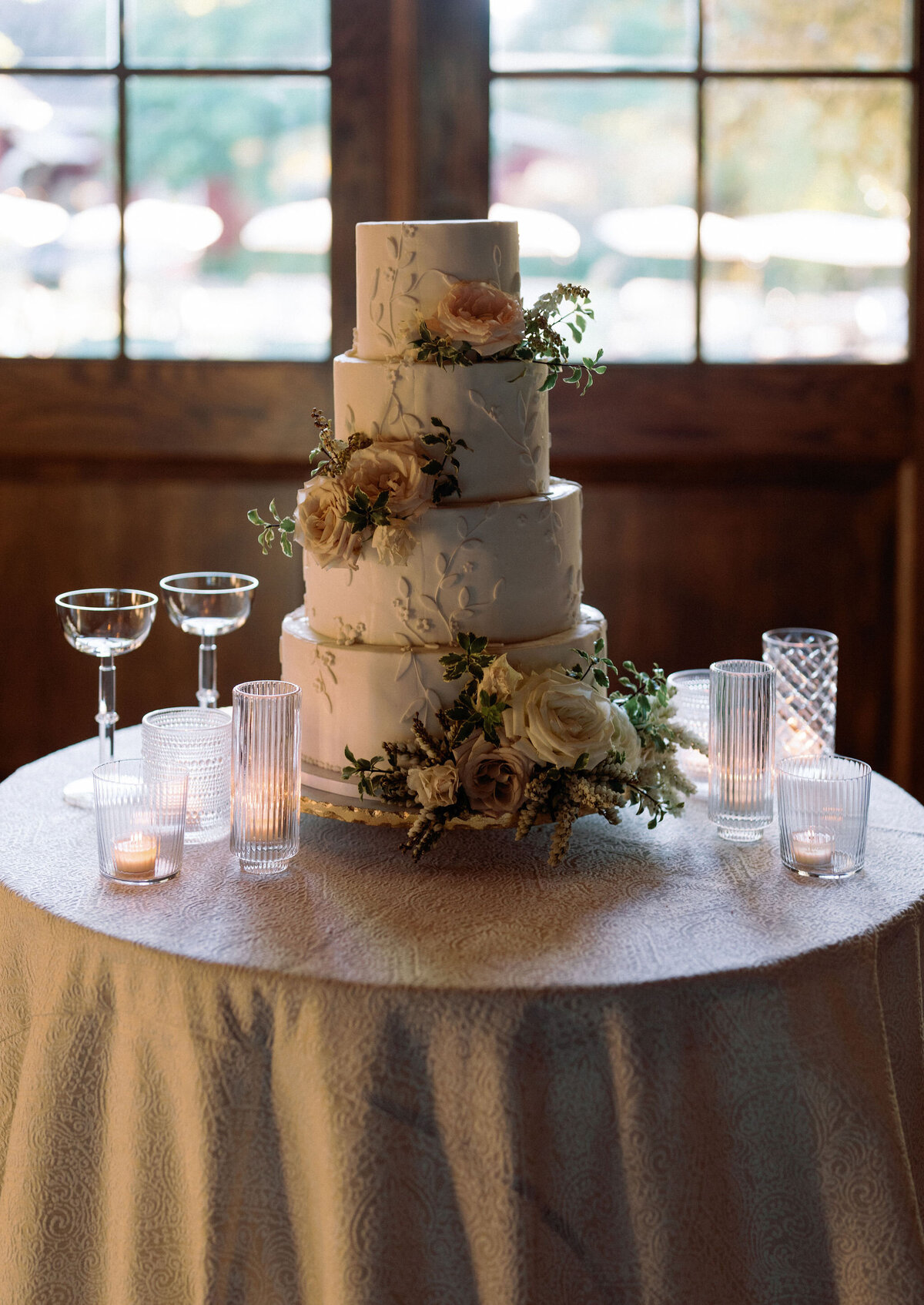 Elegant wedding cake design with four layers and adorned with florals. Lush rose garden inspired wedding design in hues of cream, white, blush, and natural greens. Fall wedding at Blackberry Farm. Timeless wedding cake design. Design by Rosemary & Finch Floral Design in Nashville, TN.