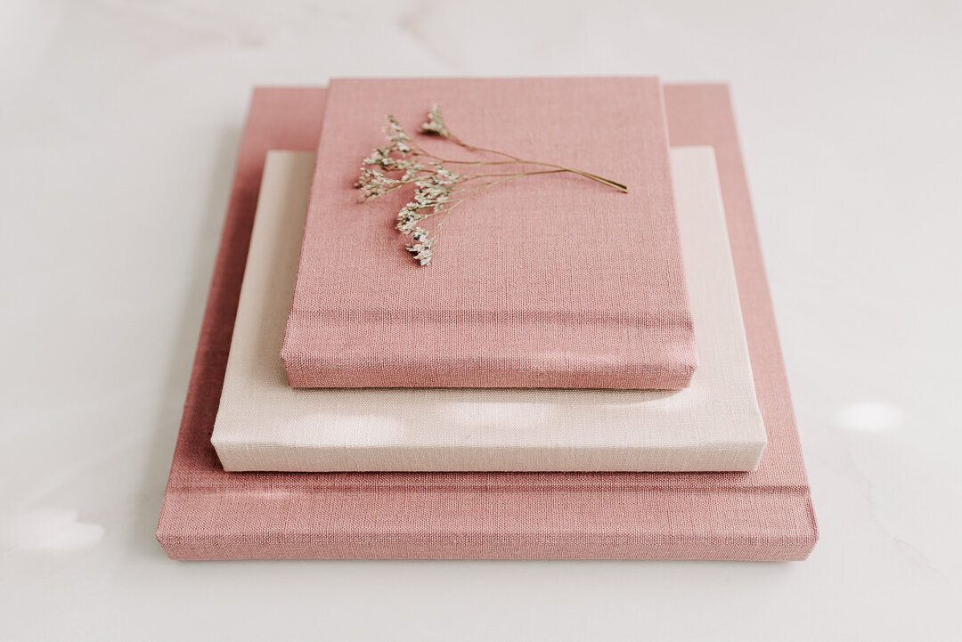 A stack of cream and blush heirloom linen albums and folios