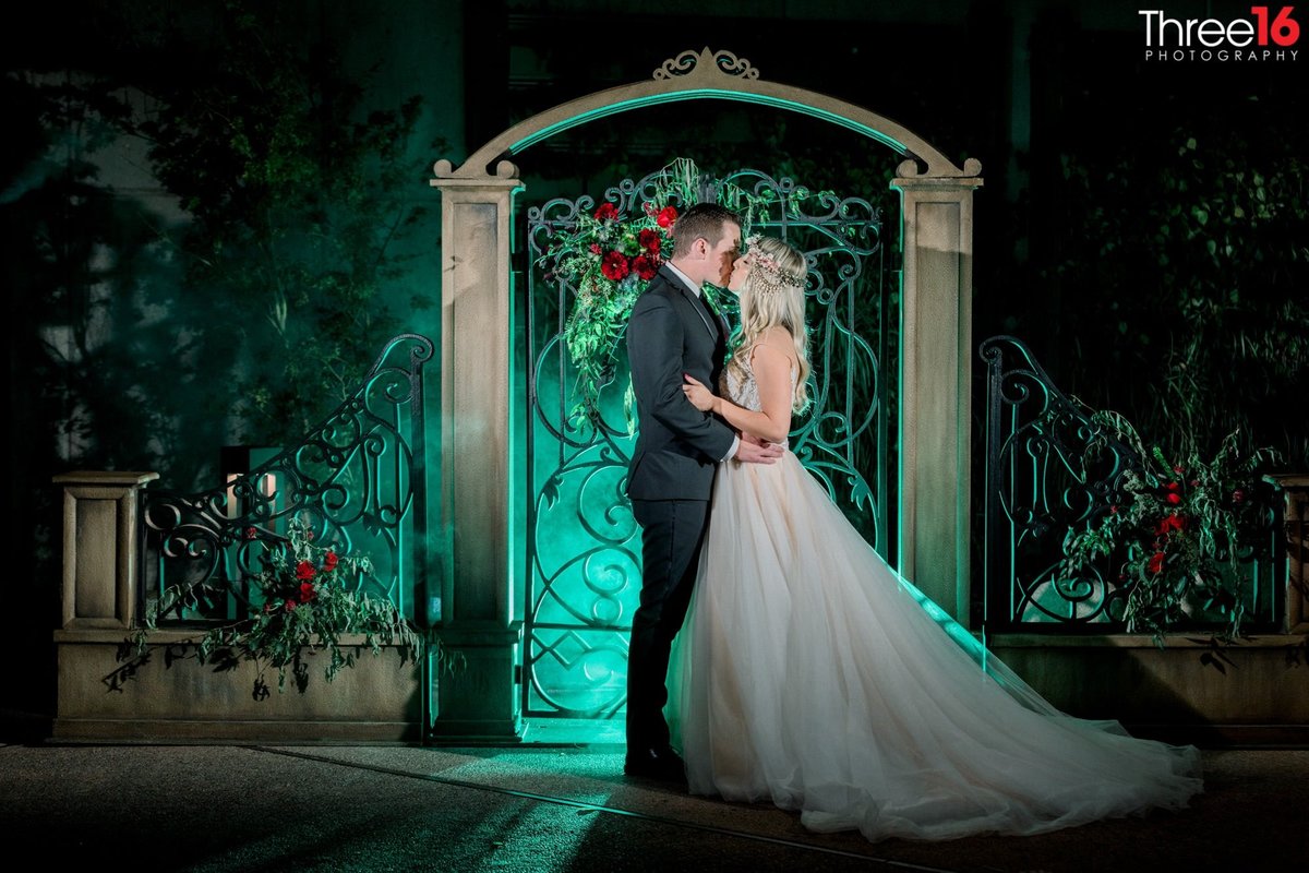 Bride and Groom share an evening kiss outside the gate with a greenish glow behind them
