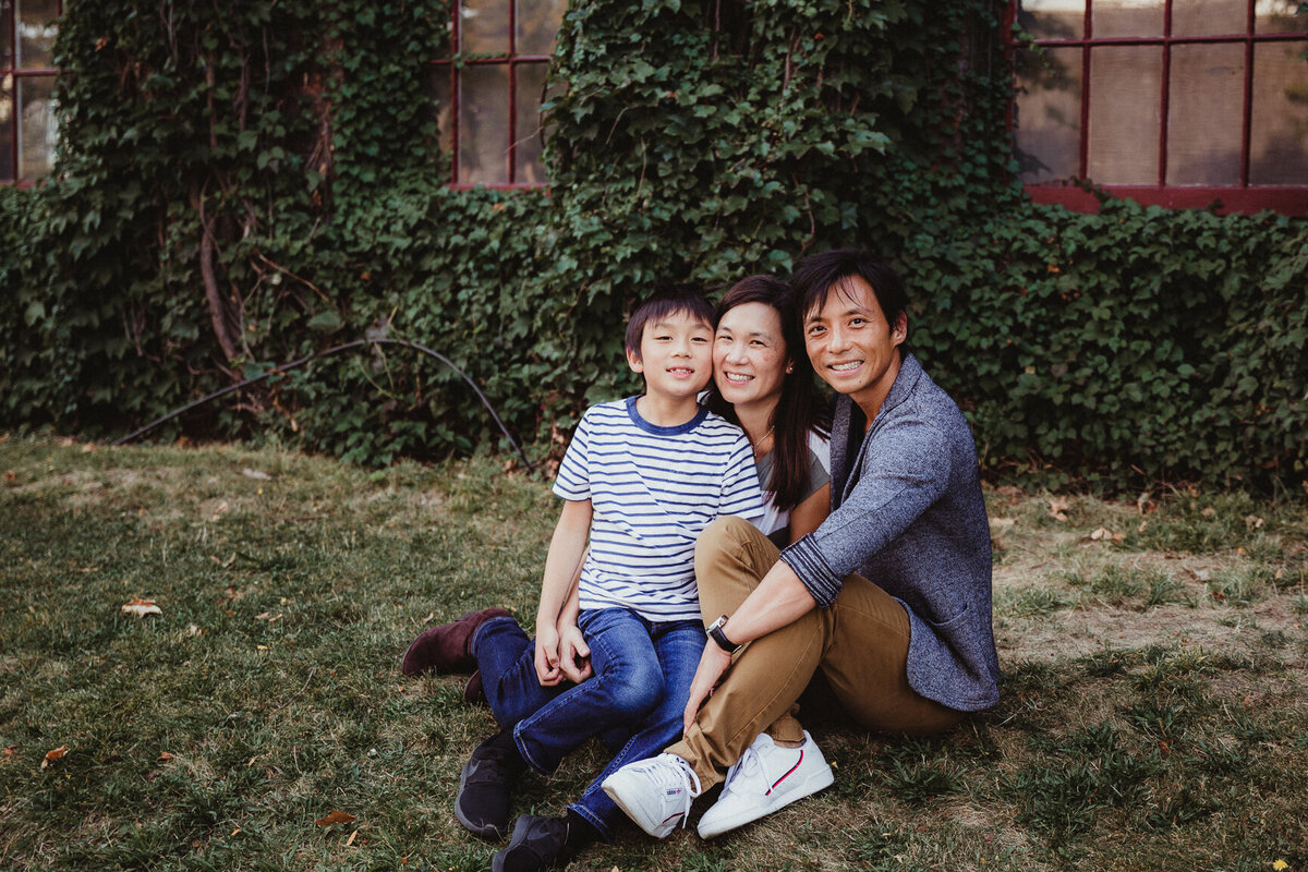 Family of 3 sitting in front of ivy covered building