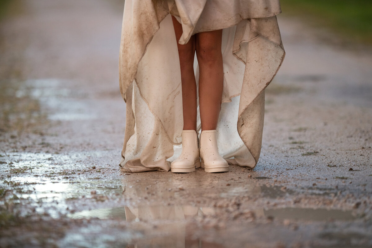 Bride in white rain boots getting ready to jump in a rain puddle