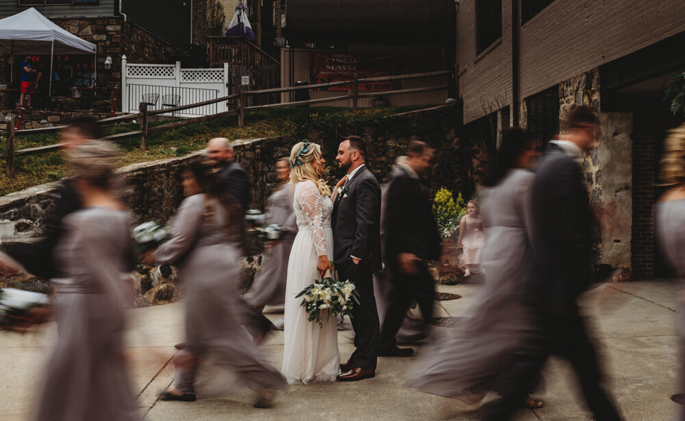 Unique bridal party photo with bride and groom standing together as their bridal party passes in a blur photographed by Maryland wedding photographer